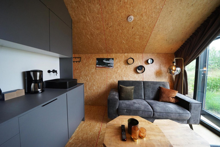 Lodge moderno en Solo Retreat, Bad Hulckesteijn, Países Bajos, con sofá gris y cocina integrada.