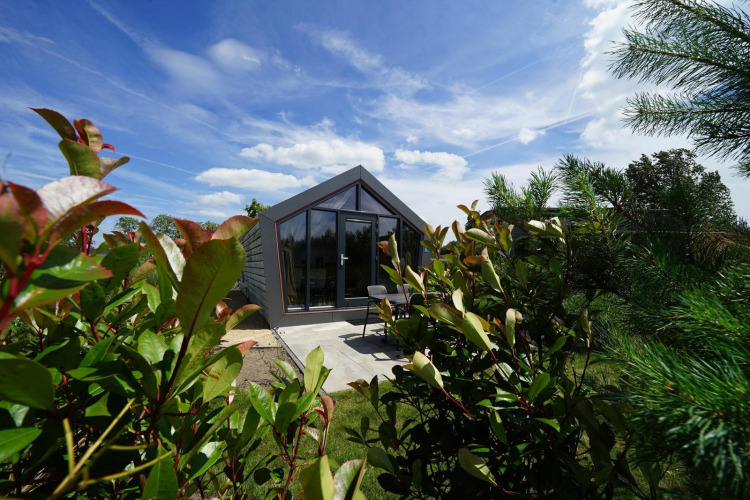 Moderna cabaña Solo Retreat en Bad Hulckesteijn, Países Bajos, rodeada de vegetación y cielo azul claro.