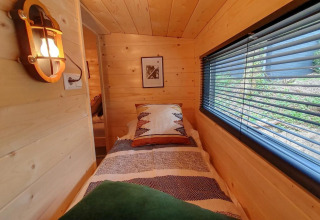 Intérieur d’une tiny house à Bad Hulckesteijn, Pays-Bas, lit simple, murs en bois, grande fenêtre latérale.