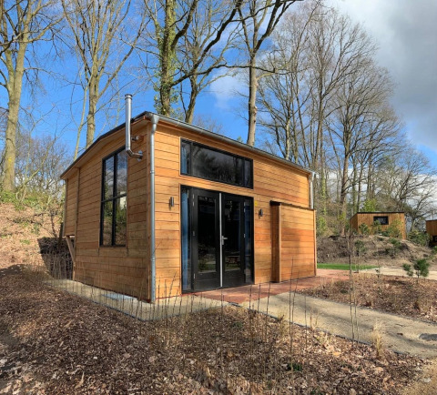 Modernes Tiny House aus Holz mit großen Fenstern im Wald bei Bad Hulckesteijn, Niederlande.