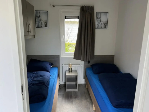 Kamer met twee eenpersoonsbedden, blauw beddengoed en raam in L-Pavilion bij Poort van Zeeland, Nederland.
