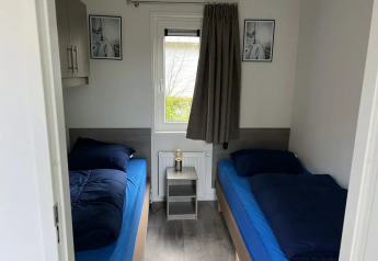 Værelse med to enkeltsenge, grå gardiner, blå sengetøj og lille natbord i L-Pavilion ved Poort van Zeeland.