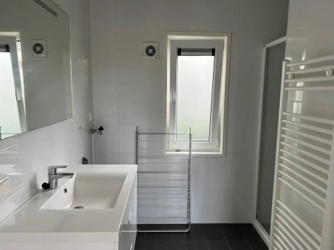 Badkamer in L-Pavilion bij Poort van Zeeland met wastafel, spiegel, raam, douche en handdoekradiator.