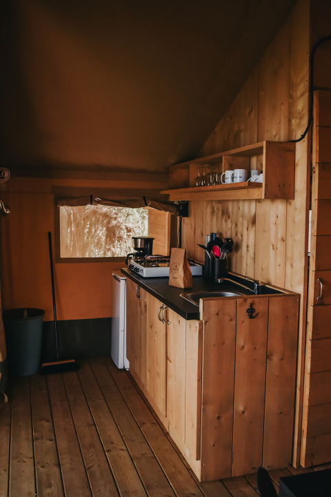 Zona de cocina en una tienda safari del Camping Luna del Monte en Italia, con interior de madera y utensilios.