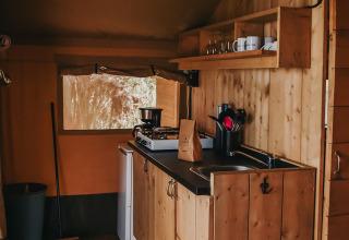 Zona de cocina en una tienda safari del Camping Luna del Monte en Italia, con interior de madera y utensilios.