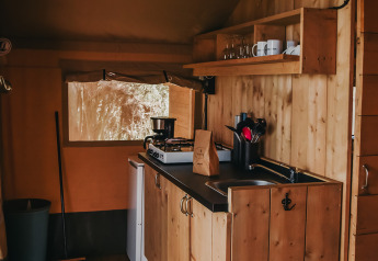 Coin cuisine d'une tente safari au Camping Luna del Monte, Italie, avec intérieur en bois et équipements.