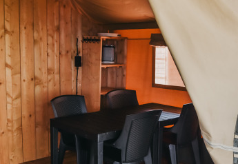 Vista interior de la tienda Safari con mesa de comedor y sillas de plástico en Camping Luna del Monte, Italia.
