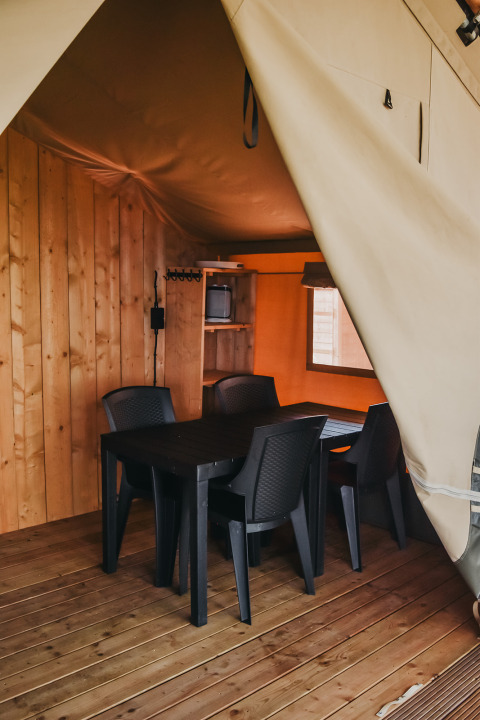 Interior view of Safari tent with dining table and plastic chairs at Camping Luna del Monte in Italy.