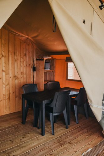 Vista interior de la tienda Safari con mesa de comedor y sillas de plástico en Camping Luna del Monte, Italia.