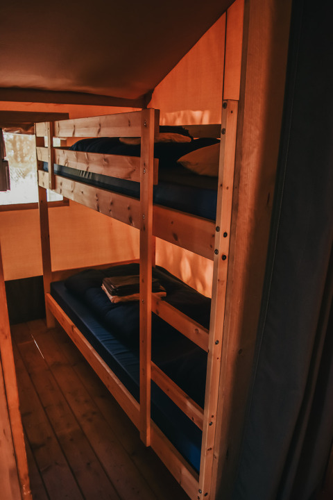 Interior view of a safari tent lodge with wooden bunk beds at Camping Luna del Monte, Italy.