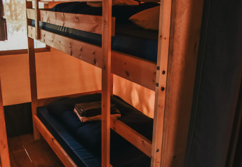 Vista interior de una tienda safari con literas de madera en Camping Luna del Monte, Italia.