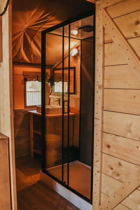 Interior view of a safari tent with private bathroom and shower at Camping Luna del Monte, Italy.