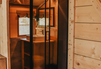 Vista interior de una tienda safari con baño privado y ducha en Camping Luna del Monte, Italia.