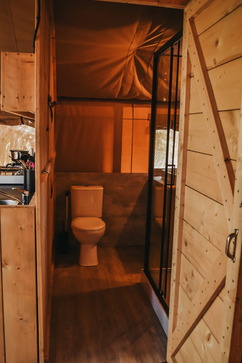 Bathroom with toilet and shower inside a safari tent with private facilities at Camping Luna del Monte, Italy.