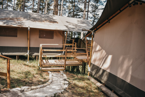 Safari tent with wooden deck and walkway at Camping Luna del Monte, surrounded by tall trees in Italy.