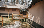 Safaritent met houten terras en wandelpad bij Camping Luna del Monte, omgeven door hoge bomen in Italië.