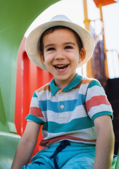Niño sonriente con sombrero jugando en un tobogán verde en un parque de vacaciones con glamping.