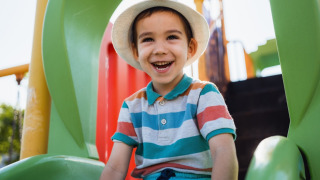 Niño sonriente con sombrero jugando en un tobogán verde en un parque de vacaciones con glamping.