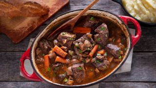 En gryde med simreret, grøntsager og brød på skærebræt, serveret ved siden af kartoffelmos på en rustik træbord.