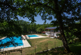 Zicht op zwembaden en hoofdgebouw van Camping Etxarri vakantiepark in Navarra, Spanje, omringd door bomen.