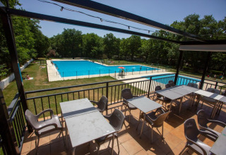 Blick von einer Terrasse mit Tischen und Stühlen auf ein Schwimmbad im Camping Etxarri, Navarra, Spanien.