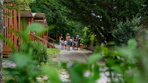 Familia con niños y perro junto a cabañas de madera en Camping Etxarri, Navarra, España, rodeados de naturaleza.