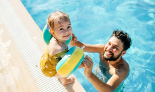 Klein kind met zwembandjes lacht aan de rand van het zwembad in een glamping vakantiepark.