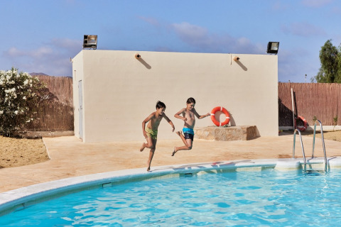 Dos niños saltan felices a la piscina en el parque vacacional TAIGA Almeria Playa en Andalucía, España.
