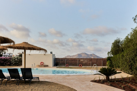 Piscina con tumbonas y sombrillas de paja en TAIGA Almeria Playa, parque vacacional, Andalucía, España.