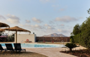 Zwembad met ligstoelen en rieten parasols bij TAIGA Almeria Playa vakantiepark, Andalusië, Spanje.
