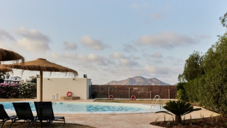 Zwembad en rieten parasols bij TAIGA Almeria Playa vakantiepark, Andalusië, Spanje, met uitzicht op bergen.