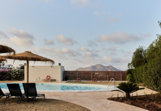 Swimming pool and straw parasols at TAIGA Almeria Playa holiday park, Andalusia, Spain, with mountain views.