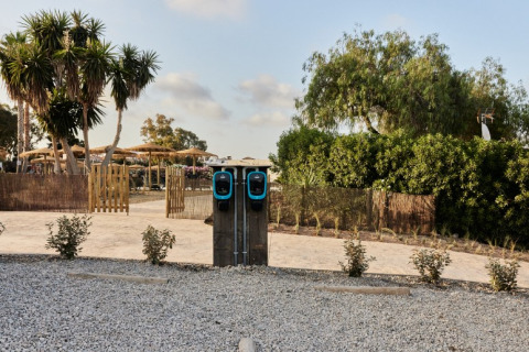 Twee laadpalen voor elektrische auto's aan TAIGA Almeria Playa vakantiepark in Andalusië, Spanje, met bomen.