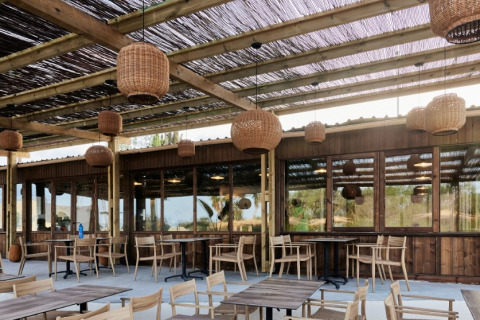 Buitenterras bij TAIGA Almeria Playa vakantiepark in Andalusië met houten meubilair en rieten lampen.