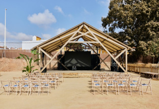 Buitenpodium met houten dak en rijen stoelen bij TAIGA Almeria Playa vakantiepark in Andalusië, Spanje.