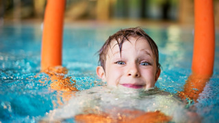 Niño sonriente en la piscina con churros de natación durante unas vacaciones glamping.