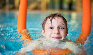 Junge schwimmt fröhlich mit Poolnudel im Wasser beim Urlaub im Glamping-Ferienpark.