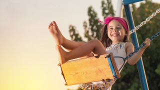 Fillette souriante avec un bandeau rose sur une balançoire dans un parc de vacances proposant du glamping.