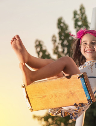 Glückliches Mädchen mit pinkem Stirnband schaukelt an einem sonnigen Tag in einem Glamping-Ferienpark.
