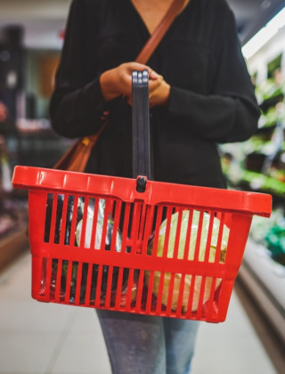 Person holding a red shopping basket in the grocery aisle at Camping l'Ardechois, Auvergne-Rhône-Alpes, France.