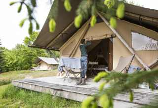 Iemand opent een glampingtent bij Huttopia Vallée de la Semois, vakantiepark te Namur, België, omringd door natuur.