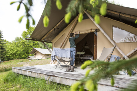 Person åbner telt på træterrasse i Huttopia Vallée de la Semois, feriepark omgivet af natur i Namur, Belgien.