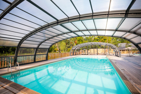 Covered indoor swimming pool with transparent roof and wooden deck at Huttopia Vallée de la Semois, Namur, Belgium.