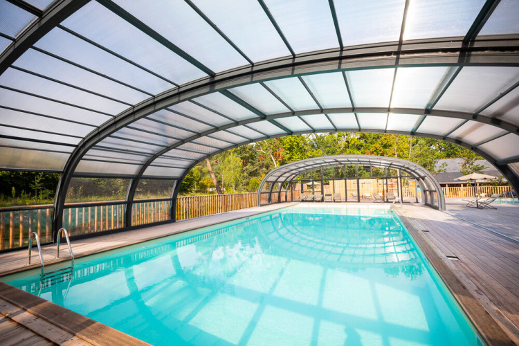 Covered indoor swimming pool with transparent roof and wooden deck at Huttopia Vallée de la Semois, Namur, Belgium.