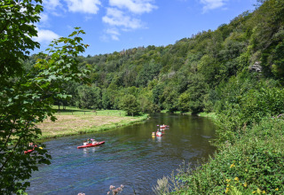Kayakers paddle on a scenic river surrounded by lush hills at Huttopia Vallée de la Semois, Namur, Belgium.