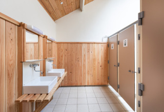 Baño con paredes de madera, dos lavabos y cabinas de inodoro en Huttopia Vallée de la Semois, Bélgica.