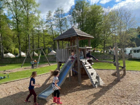 Niños jugando en un parque infantil de madera con tobogán en Huttopia Vallée de la Semois, Bélgica.