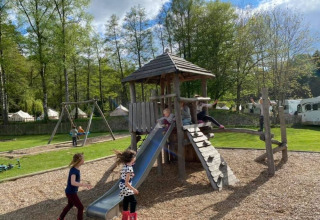Kinderen spelen op een houten speeltuin met glijbaan in Huttopia Vallée de la Semois, België.