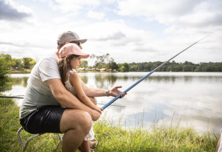 Padre e hija pescando juntos en la orilla del lago en Huttopia Vallée de la Semois, Namur, Bélgica.