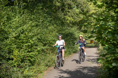 To personer cykler gennem en grøn skovsti på Huttopia Vallée de la Semois feriepark i Namur, Belgien.